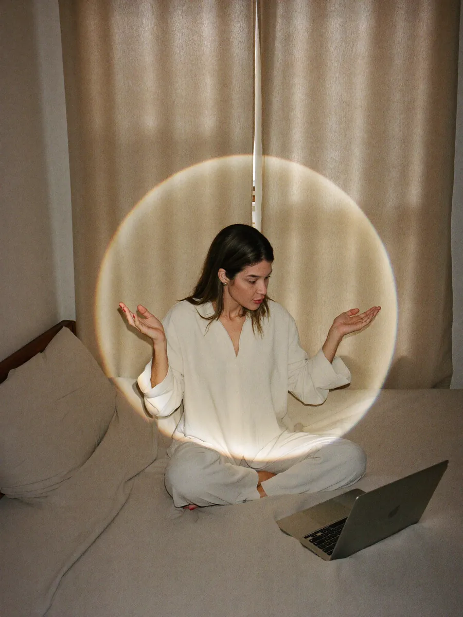 Vitoria sentada em frente ao notebook com as mãos abertas, círculos de luz dourada ao fundo