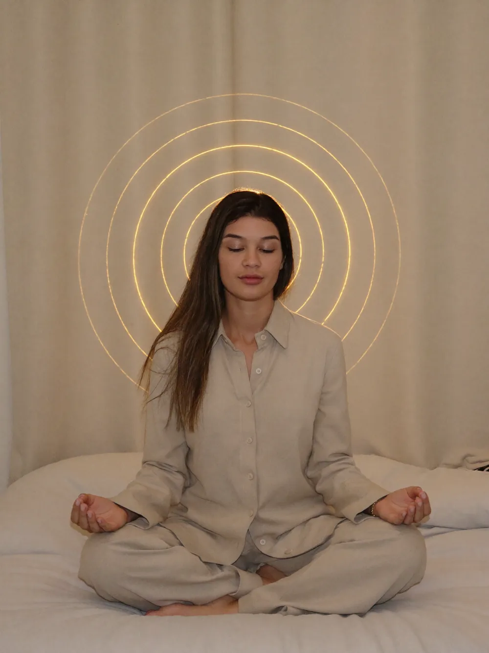Vitoria meditando de pernas cruzadas com círculos de luz dourada projetados atrás dela